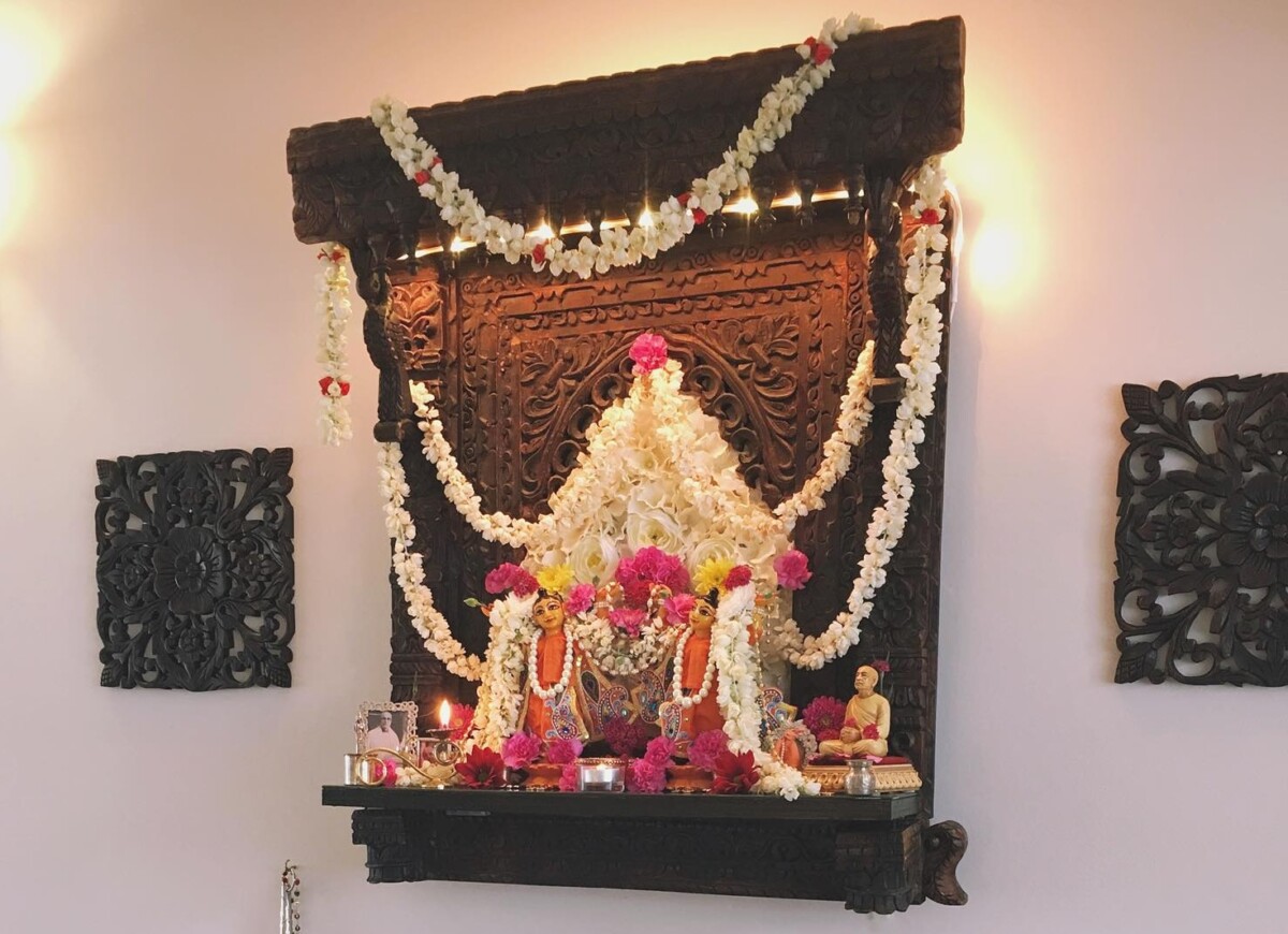 cons of Chaitanya and Nityananda stand on an ornate wooden altar mounted on the wall of a home mandir.