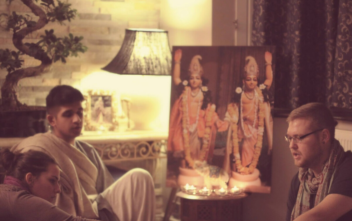 Two men and a woman, gathered in front of an image of Chaitanya and Nityananda icons, perform kirtan together.