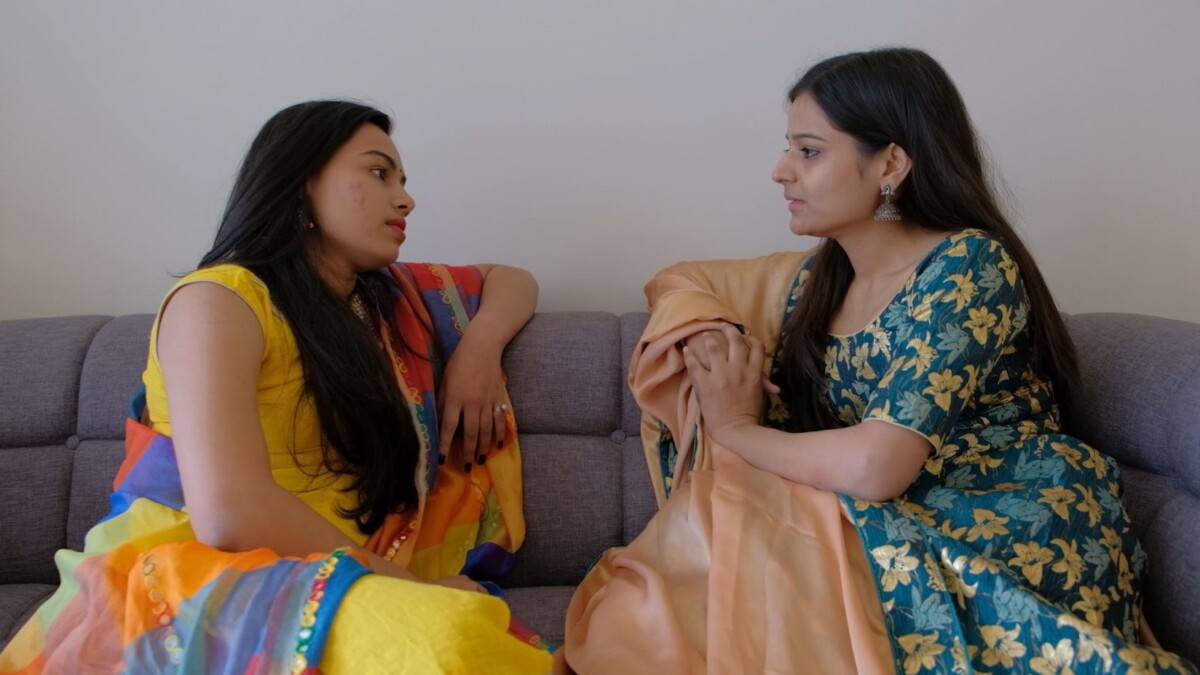 two women facing each other on a couch with serious expressions