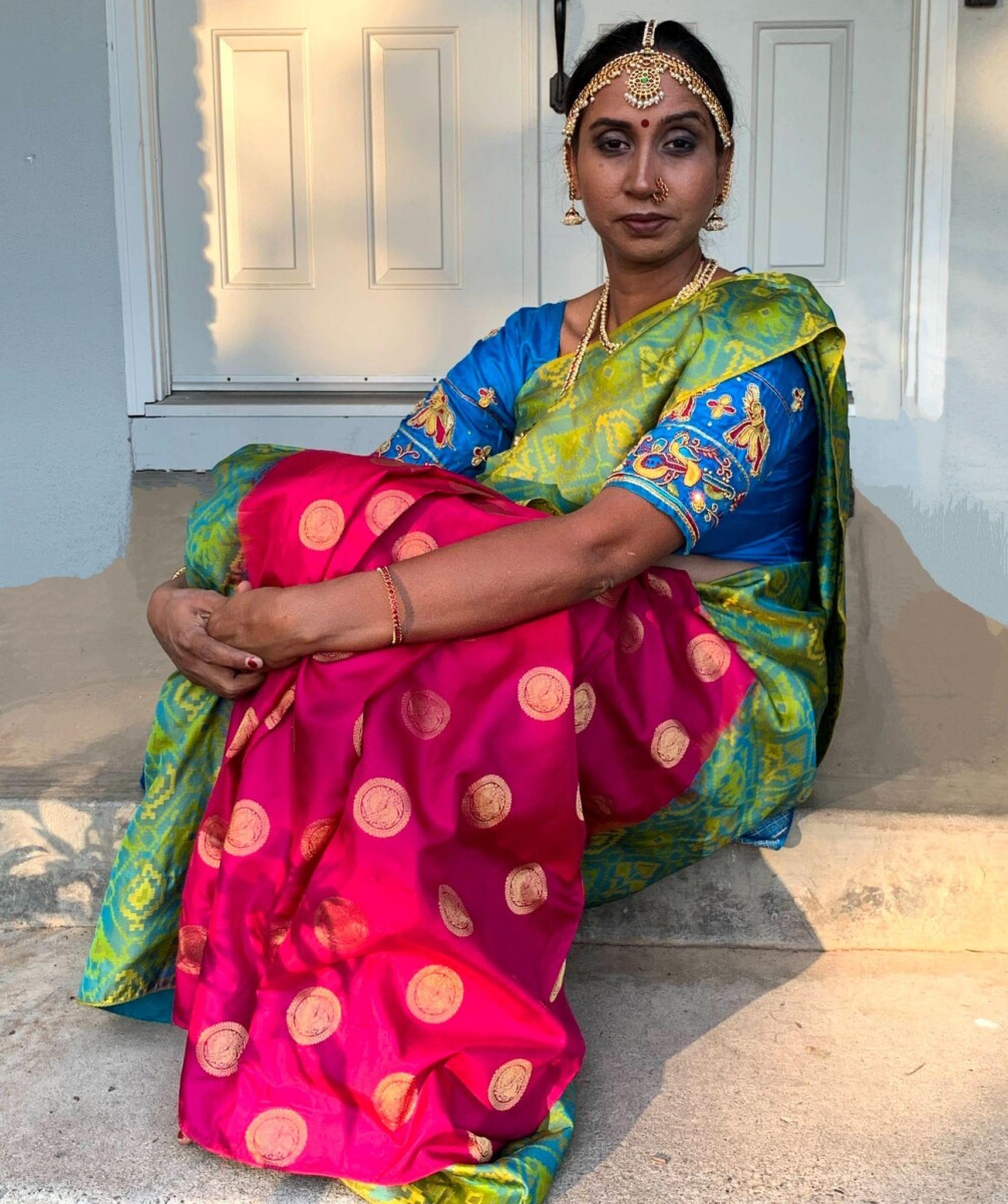 - Hindu woman poses in a green silk saree , sitting on her front porch.