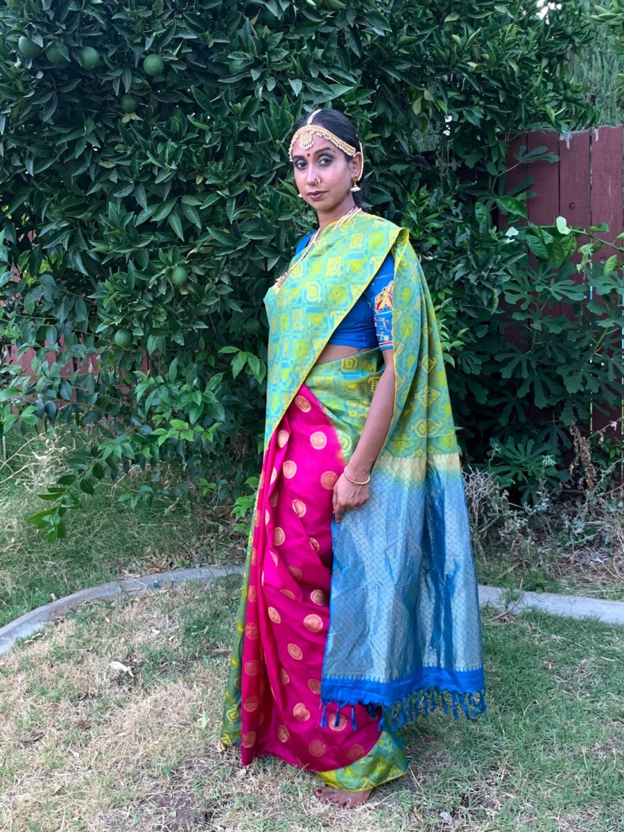 Hindu woman poses in a green silk saree, while standing in her backyard , behind an orange tree