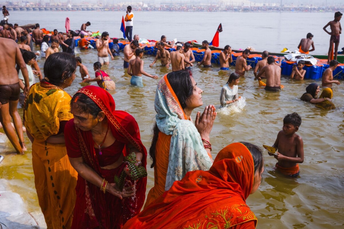 A woman praying while standing in the water at the 2025 Kumbh Mela, Prayagraj, India