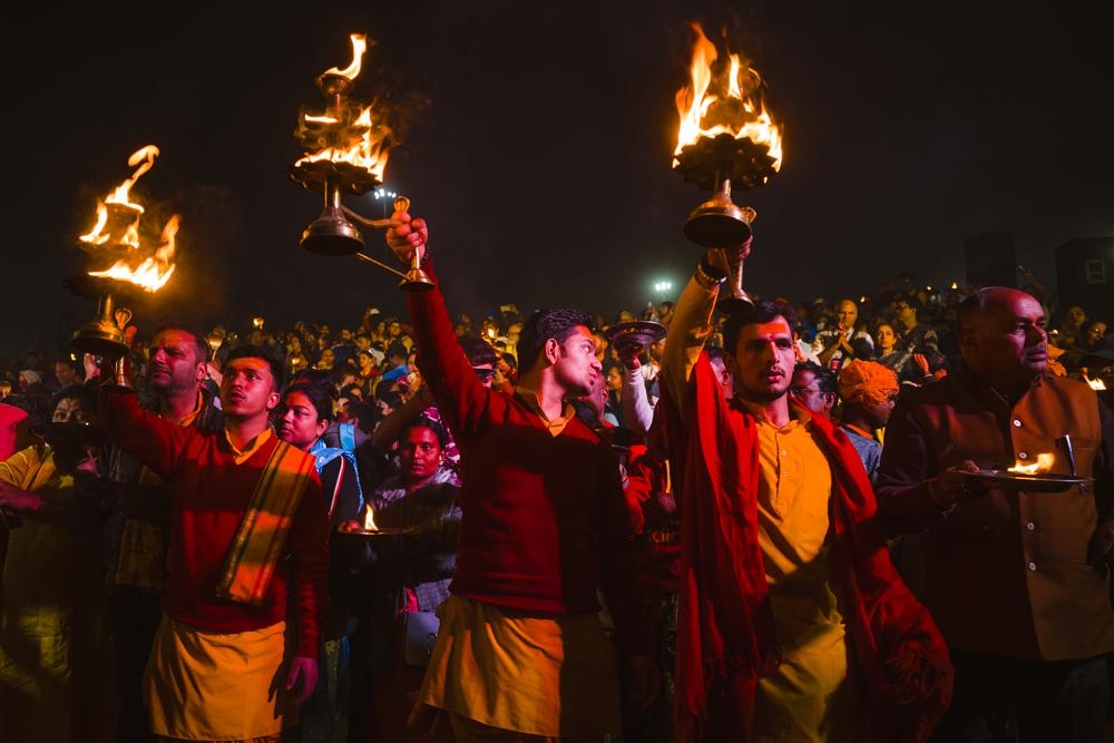 Three men wave lamps at an evening aarti at the 2025 Kumbh Mela, Prayagraj, India